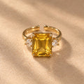 Bague Iset dorée à nano-saphir jaune rectangulaire et cristaux latéraux, posée sur un tissu beige