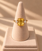 Bague Iset dorée à nano-saphir jaune rectangulaire, présentée sur un support conique beige
