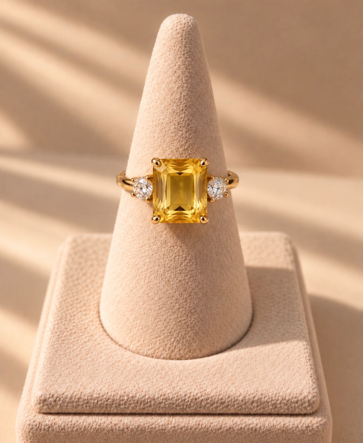 Bague Iset dorée à nano-saphir jaune rectangulaire, présentée sur un support conique beige