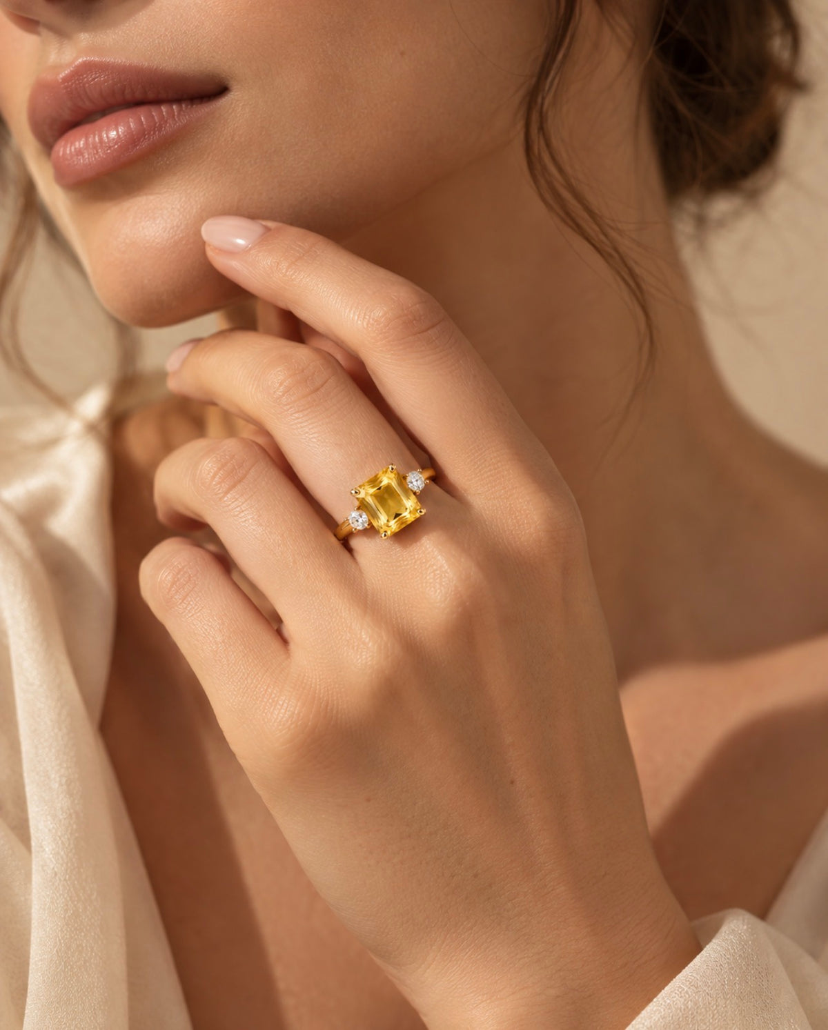 Bague Iset dorée à nano-saphir jaune et cristaux, portée à la main près du visage