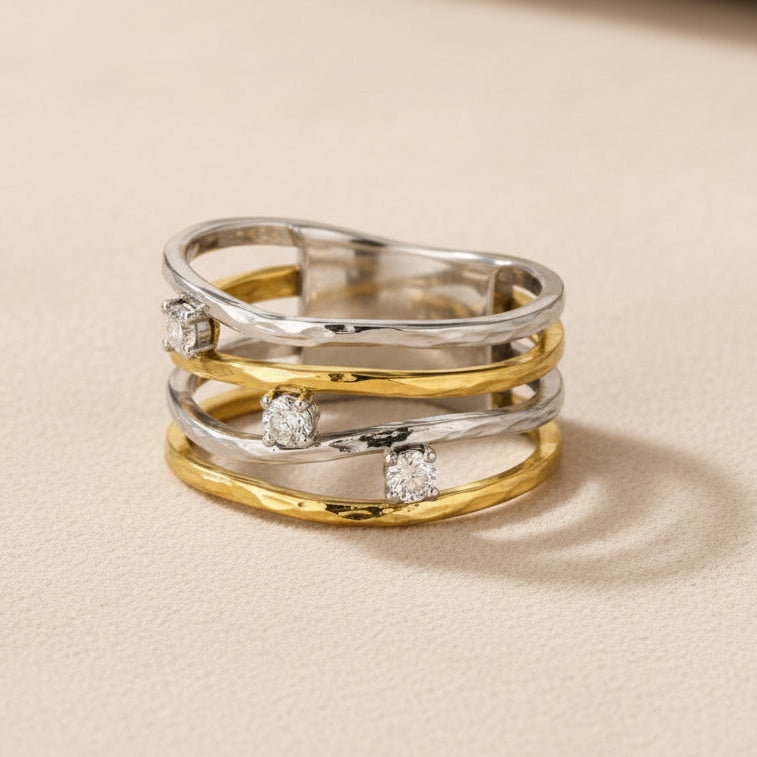 Graphique et lumineuse, cette bague bicolore joue sur l’entrelacement de lignes délicatement ondulées aux finitions dorées et argentées. Ponctuée de pierres transparentes aux reflets éclatants, elle capte subtilement la lumière et habille la mai