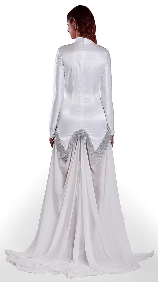 La robe Aphaïa blanche arrive à mi-cuisse suivie de son voile et est brodée à la main à partir d’un fil métallique argenté.

Col officier signé au nom de la maison, ton sur ton.

Épaules structurées avec rembourrage.

Manches longues tailleurs.

Arabesques formant des rinceaux végétaux du vie siècle s'enchaînant en bas de robe formant un demi pentagon devant et un W derrière.

Voile blanc en mousseline de soie avec transparence sur la longueur des jambes formant une traîne.

Fente centrale à l’avant jusqu’a