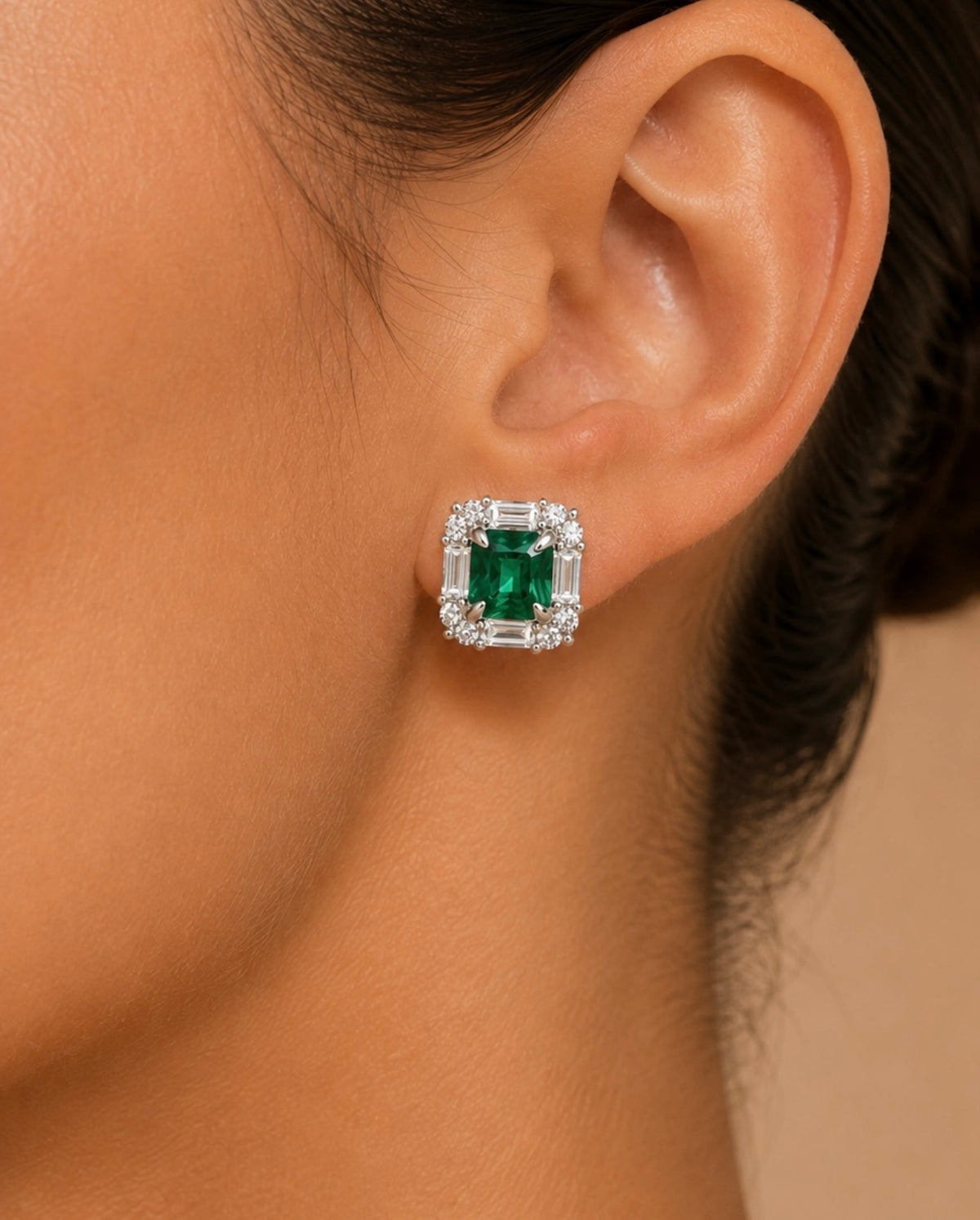 Gros plan d’une boucle d’oreille Merytamon portée, avec sa nano émeraude verte rectangulaire.