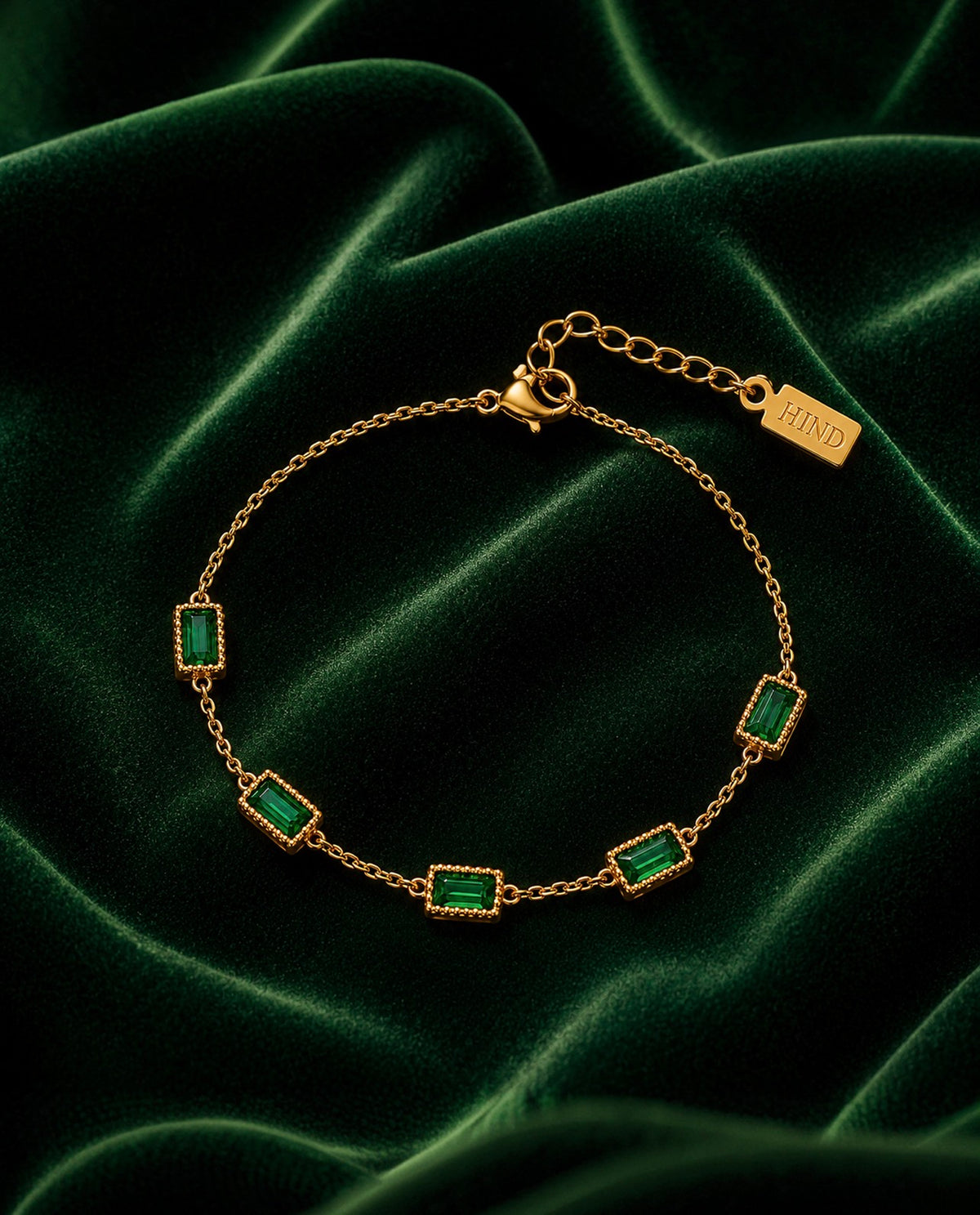 Bracelet doré à pierres vertes posé sur velours vert