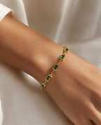 Bracelet doré fin à pierres vertes porté au poignet