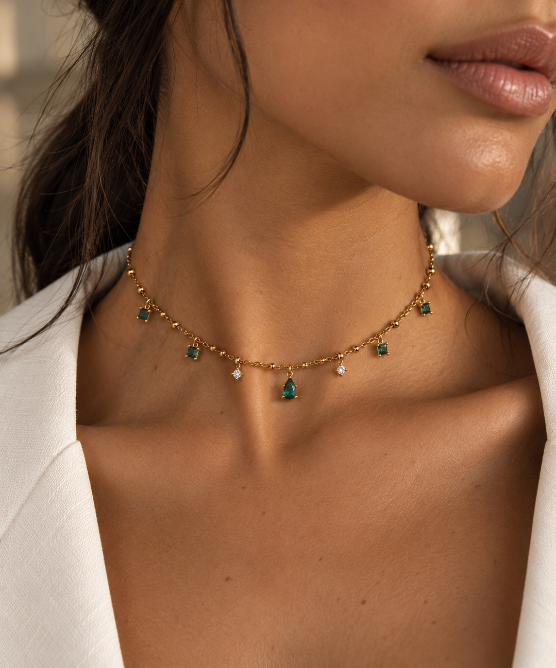 Collier Arsinoé porté, avec sa chaîne fine ponctuée de billes dorées, ses pampilles et sa goutte nano émeraude.