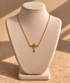 Collier Cléopâtre doré à arabesques et goutte verte présenté sur un buste ivoire