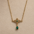 Collier Cléopâtre doré, arabesques et pendentif en goutte verte, vue de près sur fond beige