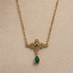 Collier Cléopâtre doré, arabesques et pendentif en goutte verte, vue de près sur fond beige