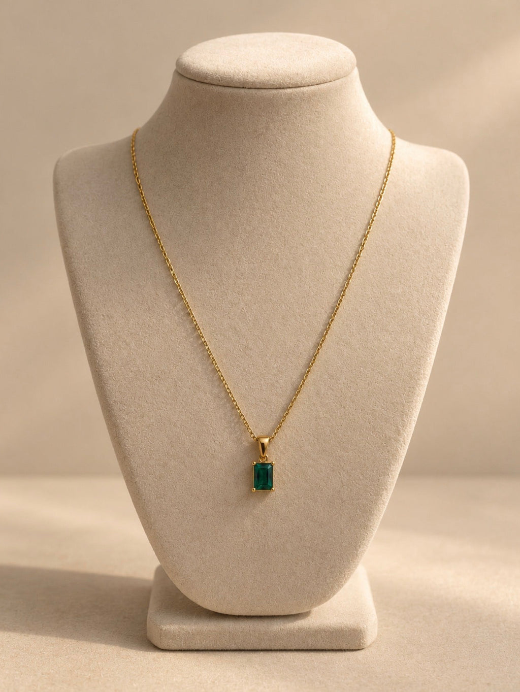 Collar dorado con colgante verde sobre busto beige