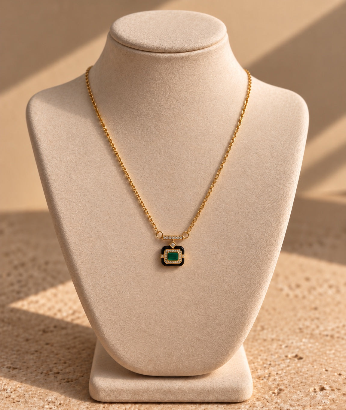 Collier ISIS doré à pendentif carré vert et noir, présenté sur un buste beige.