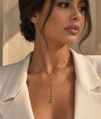 Collier Néfertari en laiton doré à l’or 18 carats porté avec une veste blanche, sa chaîne en Y soulignant le décolleté.