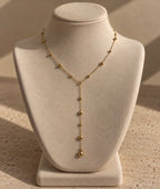 Collier Néfertari en laiton doré à l’or 18 carats, chaîne en Y ornée de boules dorées, présenté sur un buste crème.
