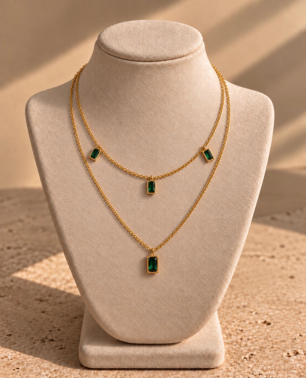 Collier Nefertiti double rang en laiton doré à l’or 18 carats et nano émeraude, présenté sur un buste crème.