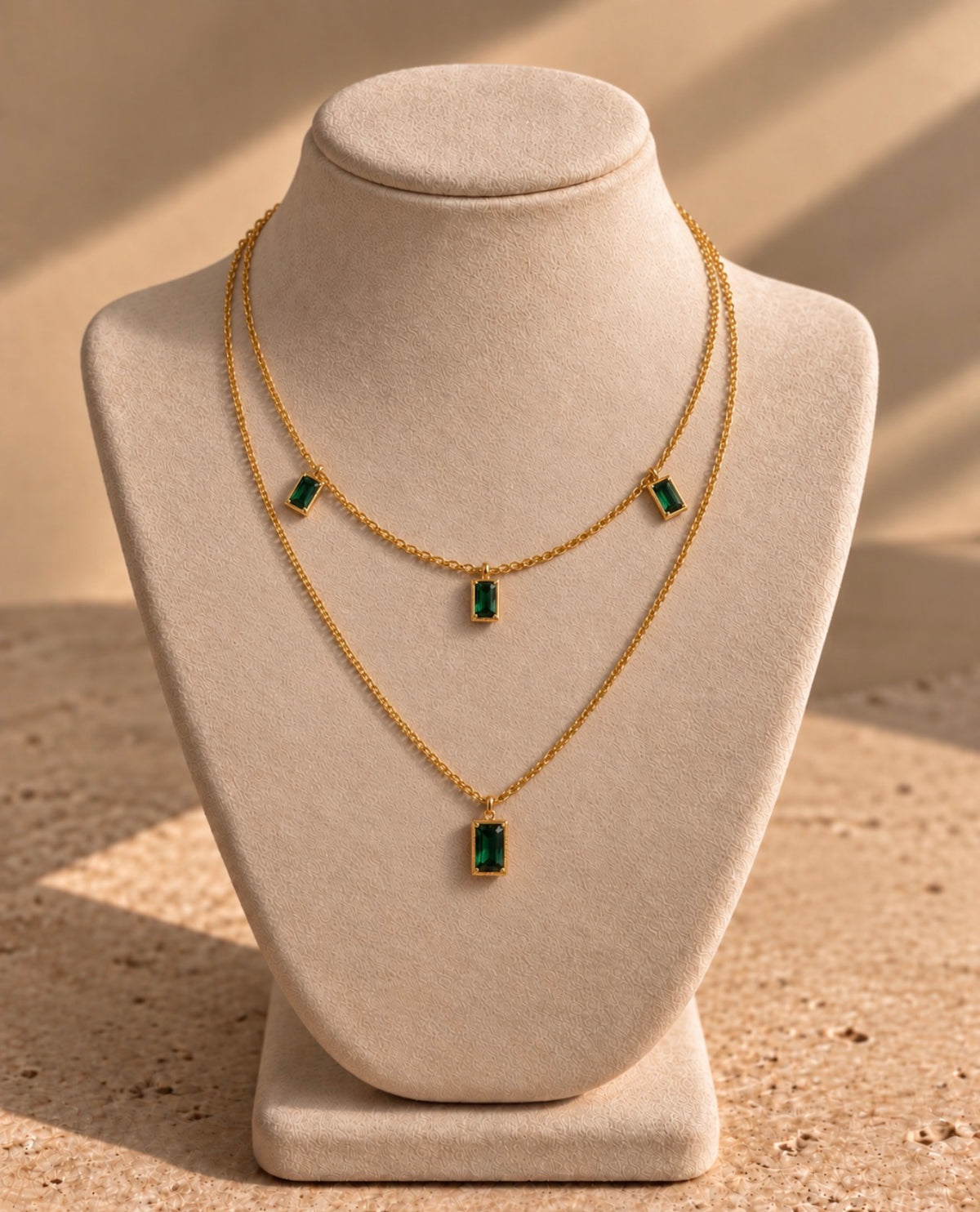 Collier Nefertiti double rang en laiton doré à l’or 18 carats et nano émeraude, présenté sur un buste crème.
