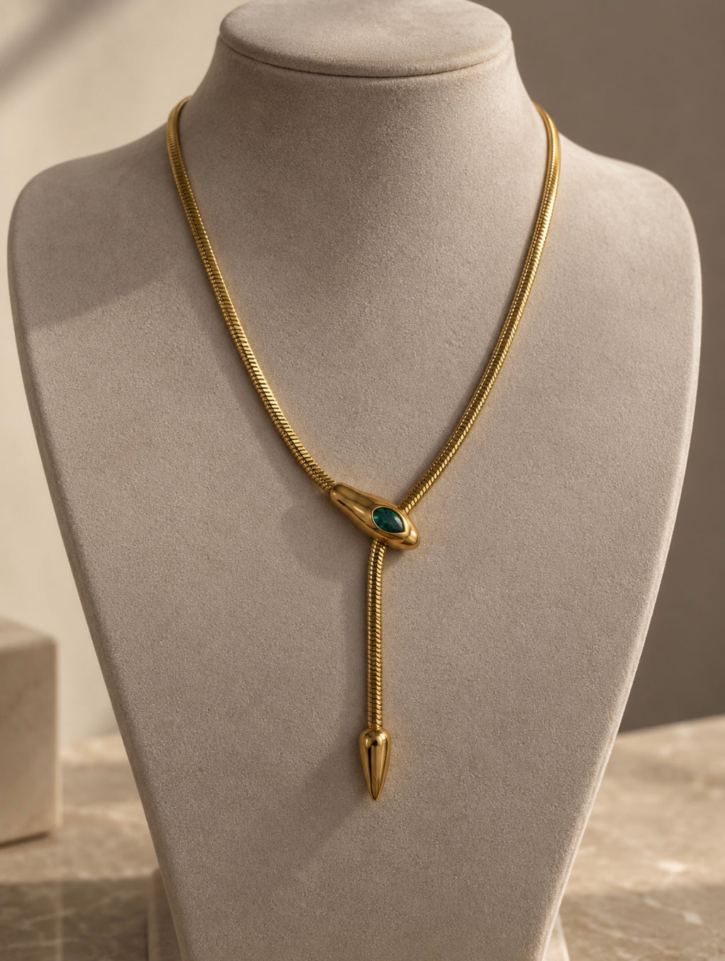 Collier serpent doré à pierre verte sur présentoir