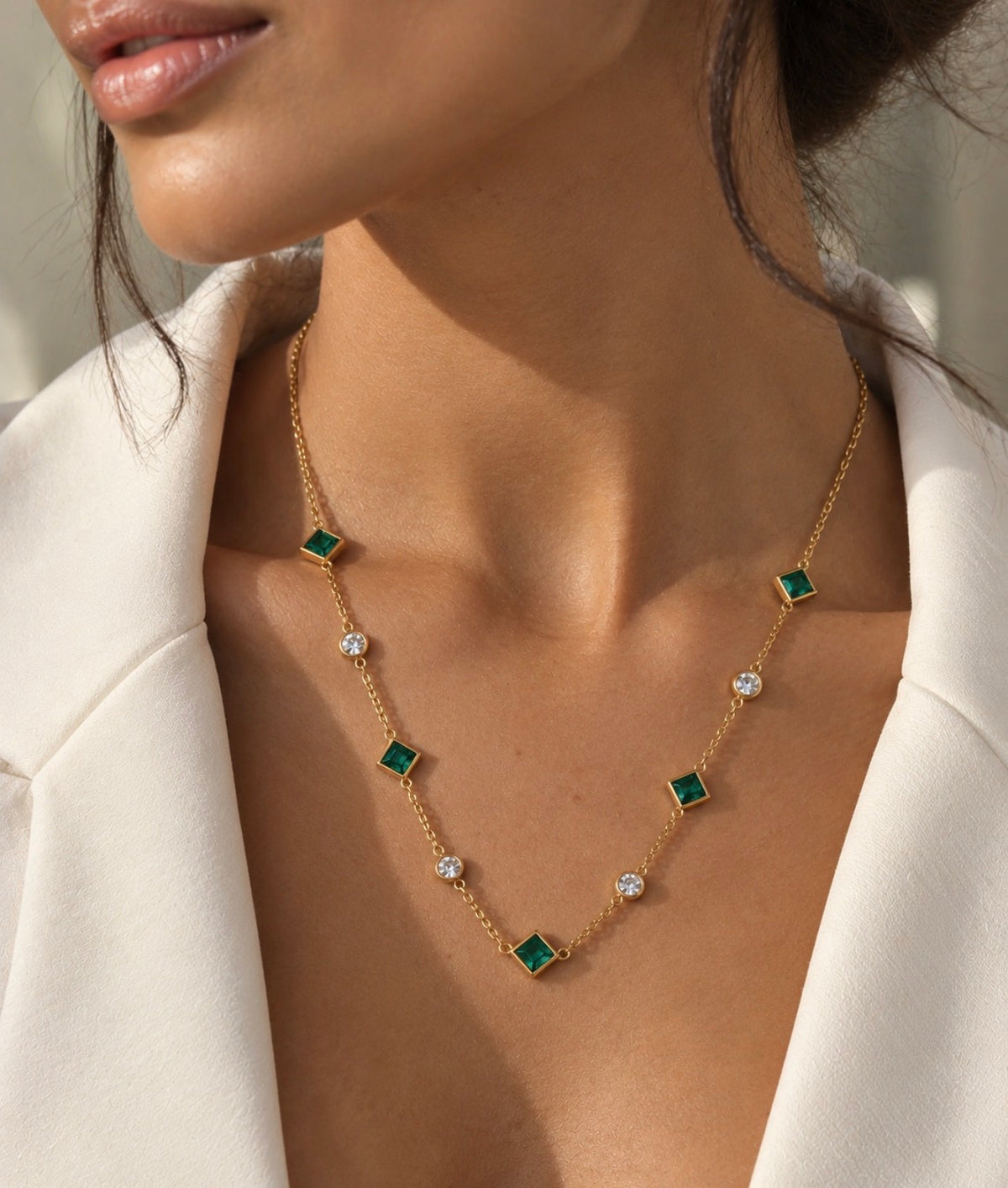 Collar Tiyi bañado en oro de 18 quilates, nanoesmeralda y cristal, en el cuello con camisa blanca.