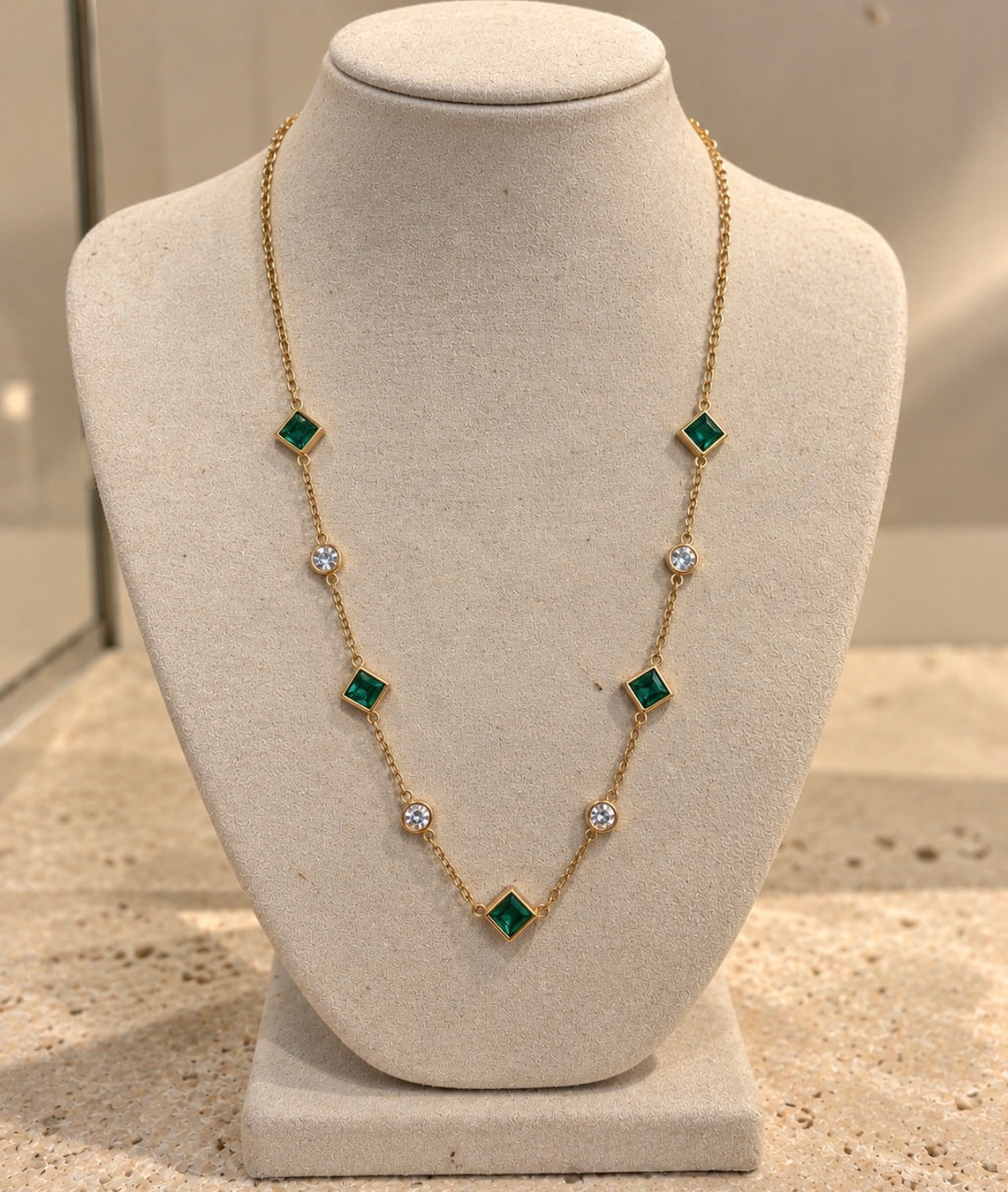 Collar Tiyi de latón bañado en oro de 18 quilates, nanoesmeralda y cristal, sobre busto crema.
