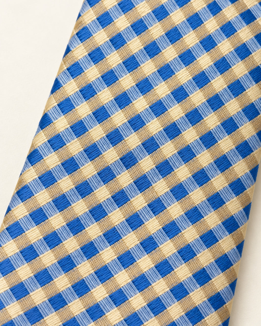 Gros plan du jacquard de soie Auber : petits carreaux bleu vif, bleu clair et champagne doré.