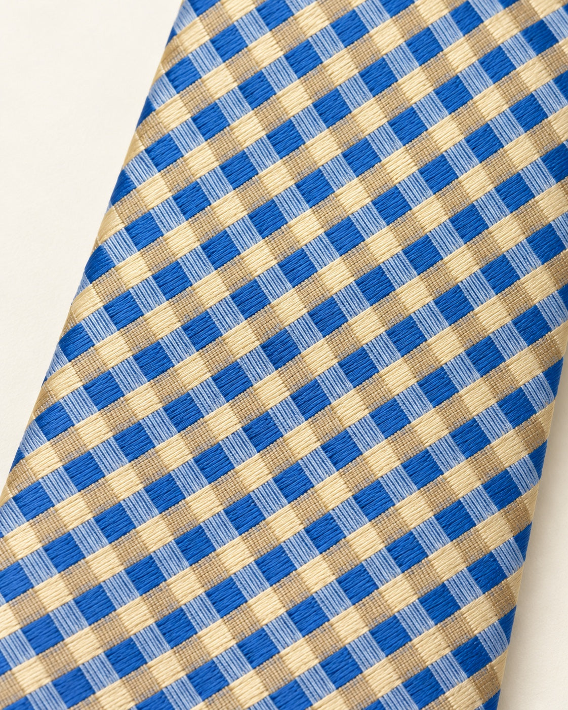 Gros plan du jacquard de soie Auber : petits carreaux bleu vif, bleu clair et champagne doré.