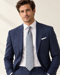 Cravate Auber à damier bleu et doré, portée avec une chemise blanche et un costume bleu marine.