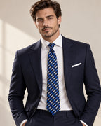Cravate Cambon à rayures bleues et blanches, portée avec un costume bleu marine, une chemise blanche et une pochette blanche.