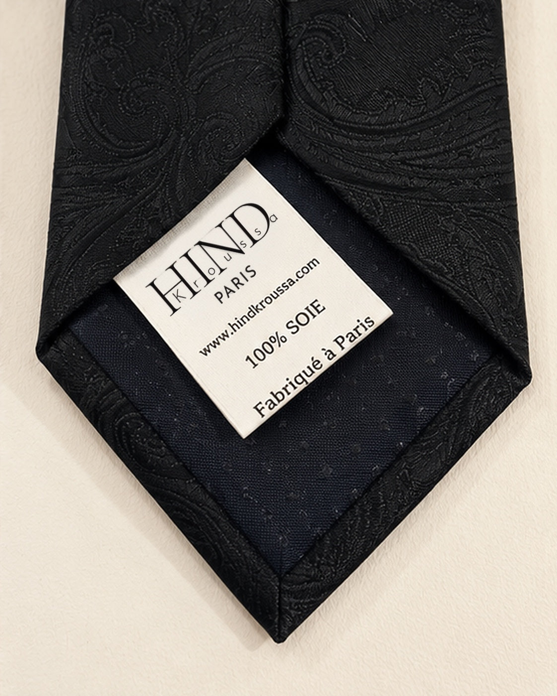 Dos de la cravate Castiglione noire, doublure sombre et étiquette Hind Kroussa Paris indiquant 100 % soie et fabriqué à Paris.