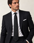 Cravate Castiglione noire à motif cachemire ton sur ton, portée avec une chemise blanche, un costume noir et une pochette blanche.