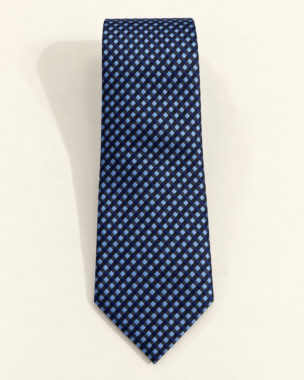 Cravate Caumartin en jacquard de soie, à petits carreaux bleu marine, bleu ciel et noirs, présentée à plat.