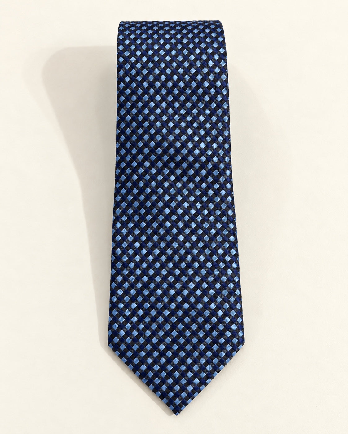 Cravate Caumartin en jacquard de soie, à petits carreaux bleu marine, bleu ciel et noirs, présentée à plat.