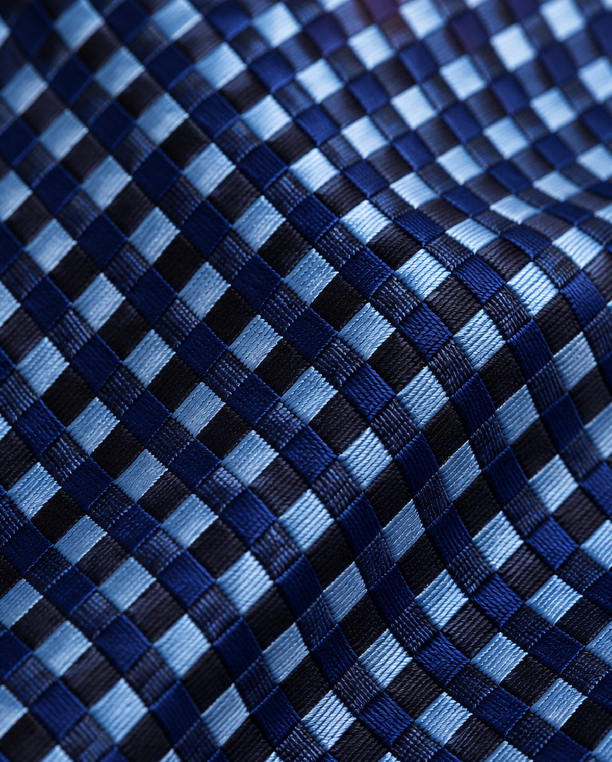 Gros plan du jacquard de soie Caumartin : damier de petits carreaux bleu ciel, bleu marine et noirs aux reflets satinés.
