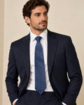 Cravate Caumartin à damier bleu marine et bleu ciel, portée avec une chemise blanche et un costume bleu marine.