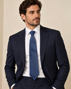 Cravate Caumartin à damier bleu marine et bleu ciel, portée avec une chemise blanche et un costume bleu marine.