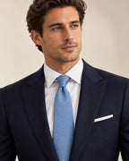 Cravate Chaptal bleu ciel texturée, portée avec un costume bleu marine, une chemise blanche et une pochette blanche.