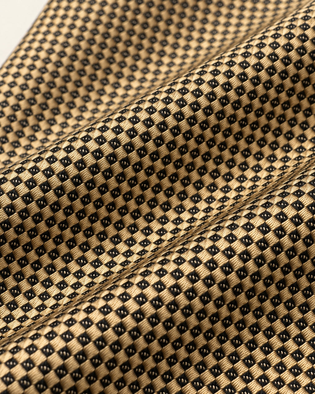 Gros plan du jacquard de soie Drouot : petits carreaux dorés et motifs noirs finement tissés.