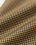 Gros plan du jacquard de soie Drouot : petits carreaux dorés et motifs noirs finement tissés.