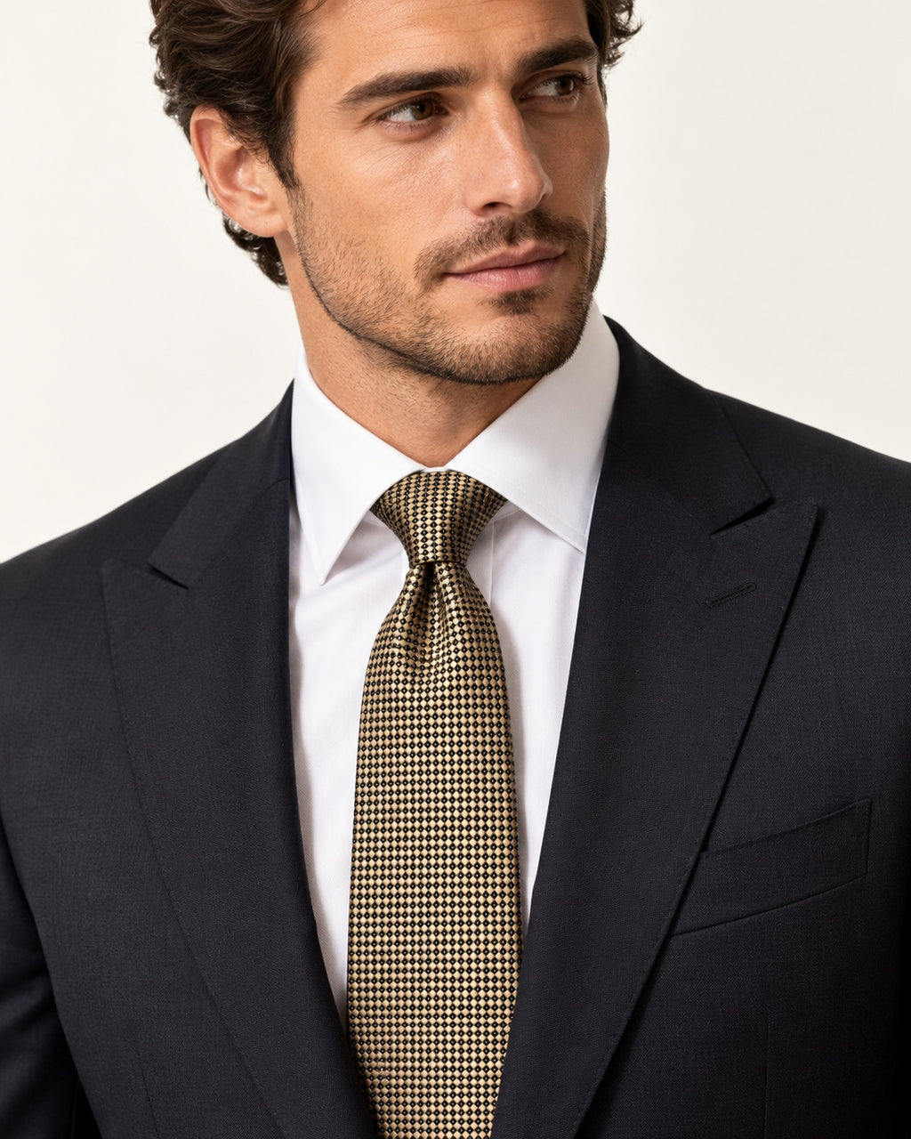 Cravate Drouot dorée à petits motifs noirs, portée avec un costume sombre et une chemise blanche.