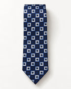 Cravate Gramont en jacquard de soie présentée à plat, ornée de carrés emboîtés bleu marine, bleu royal et gris argenté.