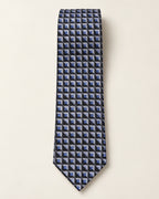 Cravate Marignan en jacquard de soie présentée à plat, à carrés bleus facettés et triangles gris argenté sur fond noir.