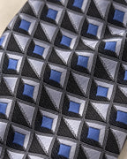Gros plan du jacquard Marignan : carrés bleus, facettes gris argenté et triangles clairs dans une grille noire texturée.
