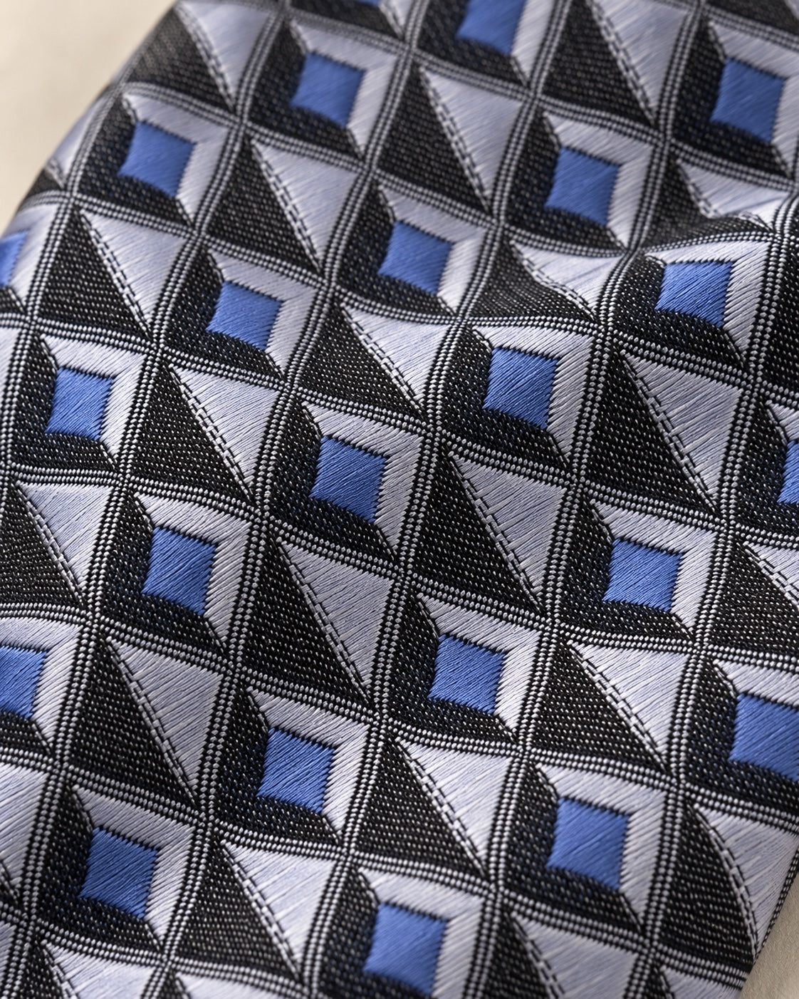 Gros plan du jacquard Marignan : carrés bleus, facettes gris argenté et triangles clairs dans une grille noire texturée.