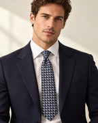 Cravate Marignan à motifs géométriques bleus, argentés et noirs, portée avec une chemise blanche et un costume bleu marine.