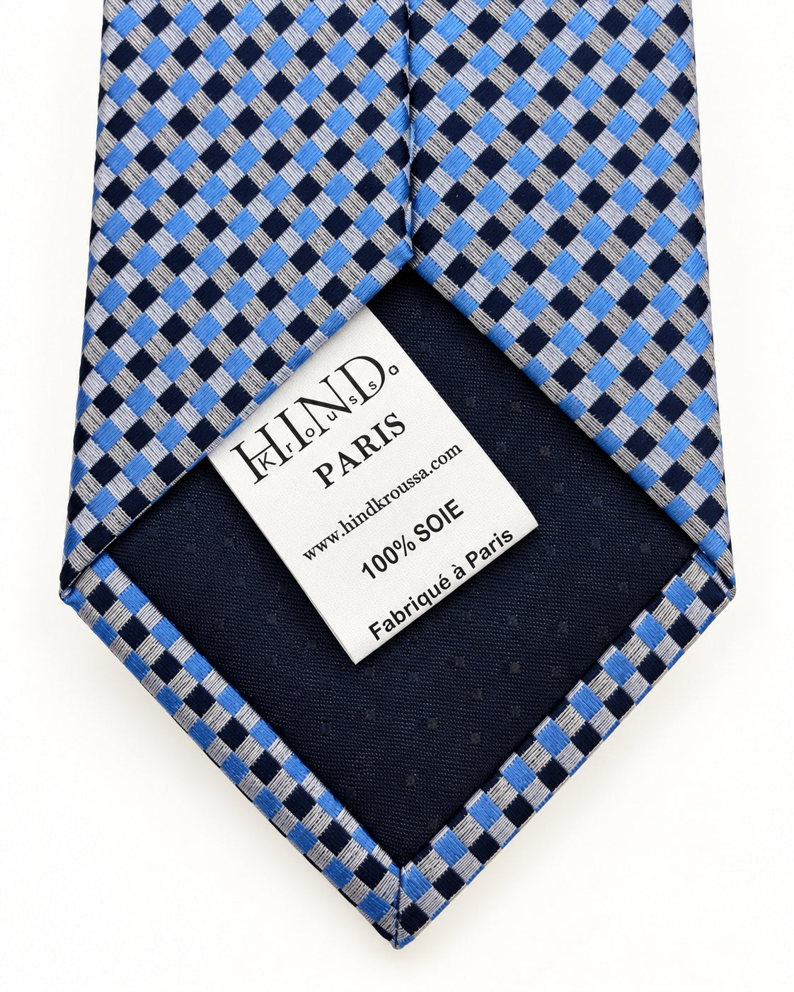 Dos de la cravate Marivaux à damier bleu, doublure marine et étiquette Hind Kroussa Paris indiquant 100 % soie.