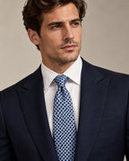 Cravate Marivaux à damier bleu ciel, marine et gris perle, portée avec un costume marine et une chemise blanche.
