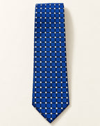 Cravate Penthièvre en soie présentée à plat, carreaux bleu royal soulignés d’une grille sombre et de petits losanges ivoire.
