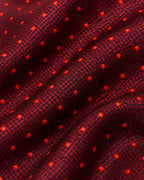 Gros plan du jacquard de soie Richelieu : micro-motifs rouges et noirs et petits pois rouge vif en relief.