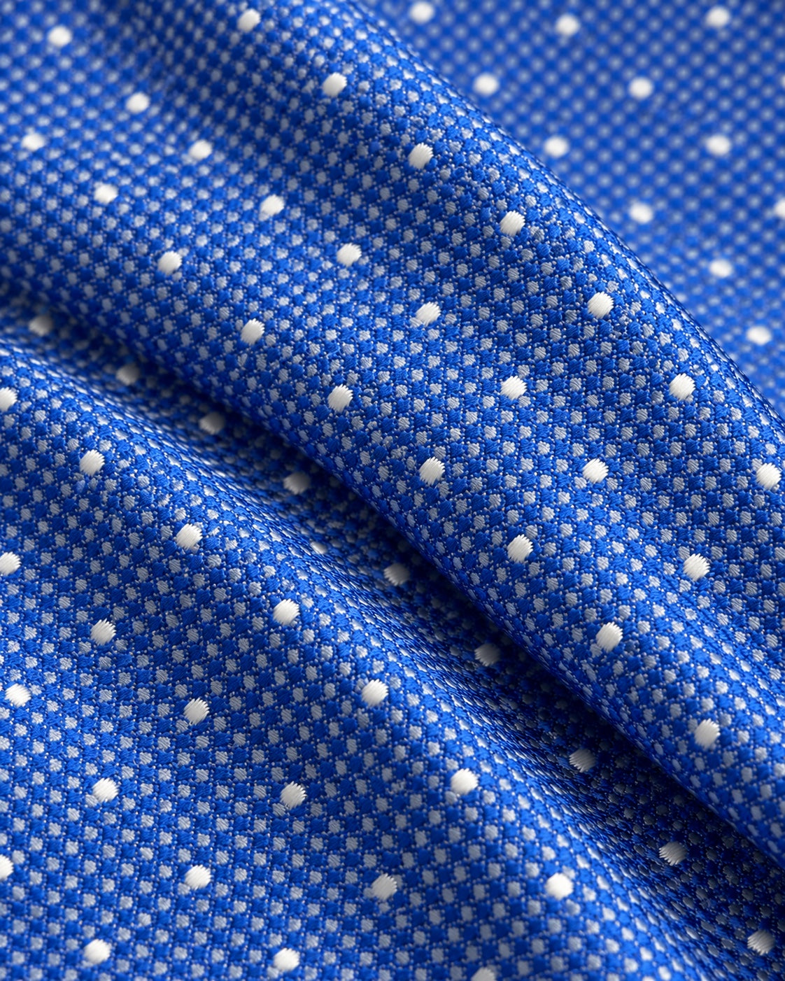 Gros plan du jacquard de soie Scribe : tissage bleu à petits motifs clairs et pois blancs en relief.