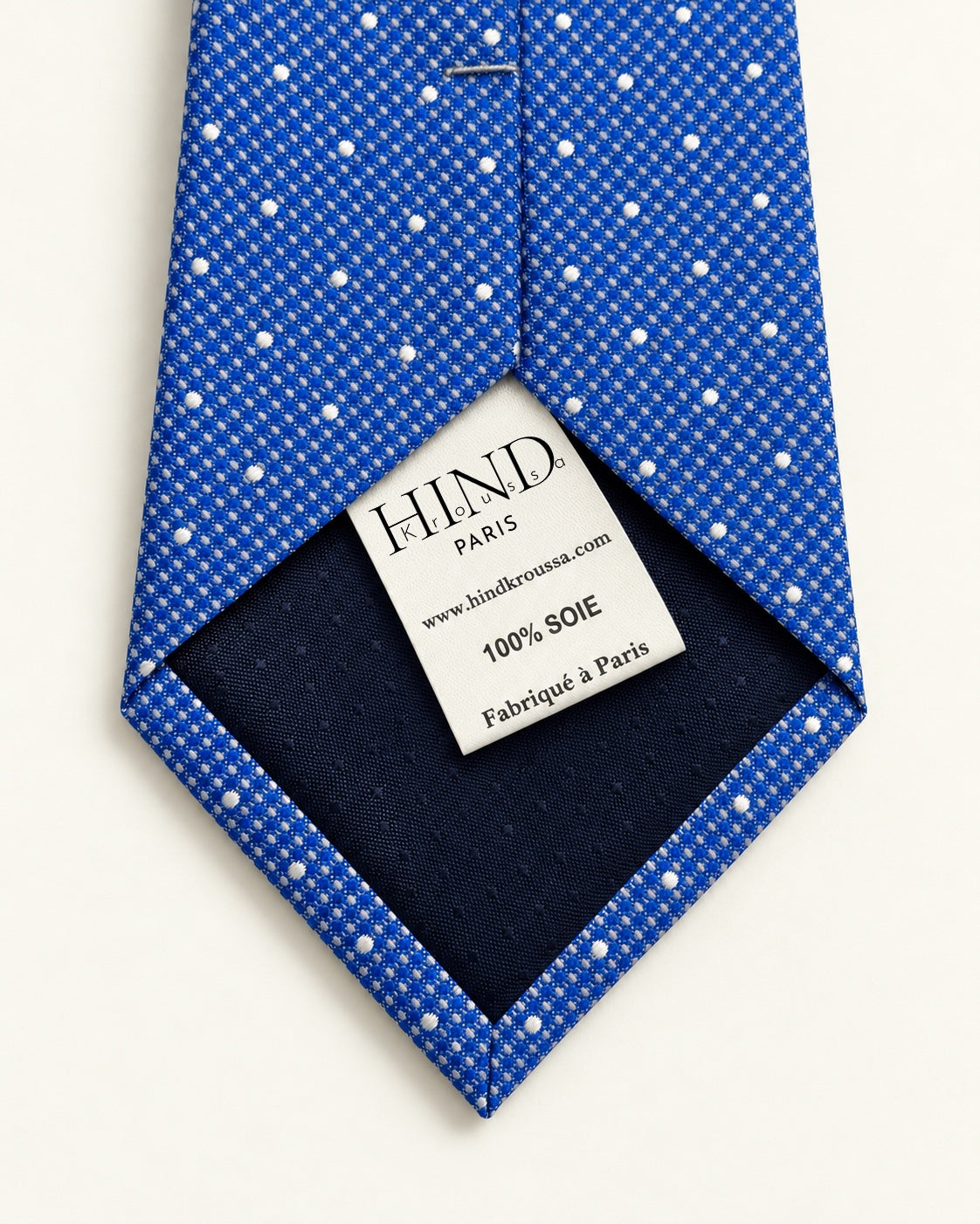 Dos de la cravate Scribe bleue à pois blancs, doublure marine et étiquette Hind Kroussa Paris, 100 % soie.