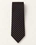 Cravate Tournon en jacquard de soie présentée à plat, alternance de pois rouges et de petits losanges blancs sur fond noir.