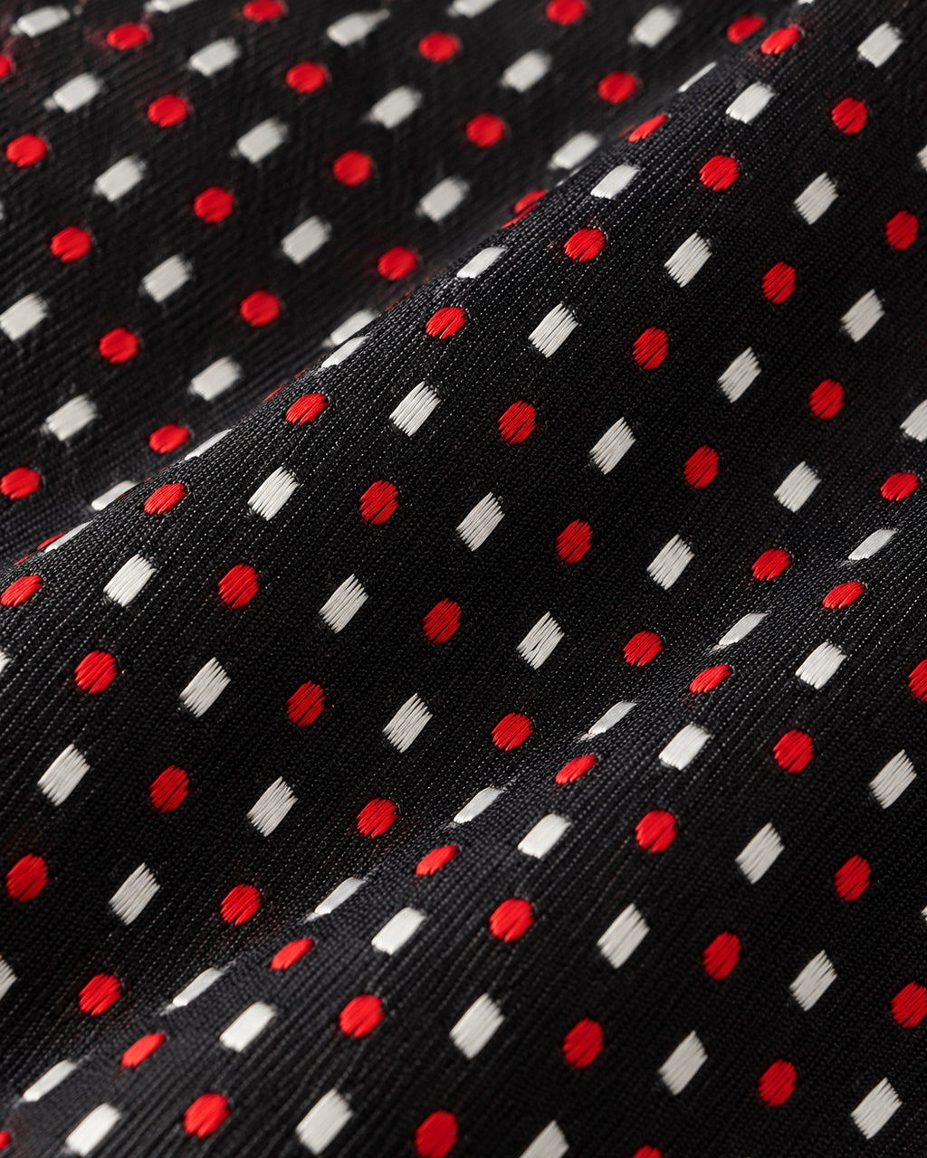 Gros plan du jacquard Tournon : pois rouges et losanges blancs tissés sur une trame noire finement texturée.